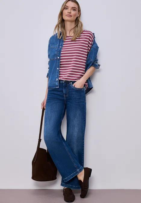 Person trägt gestreiftes T-Shirt, Jeansjacke, weite Jeans, Loafers und hält eine Tasche.